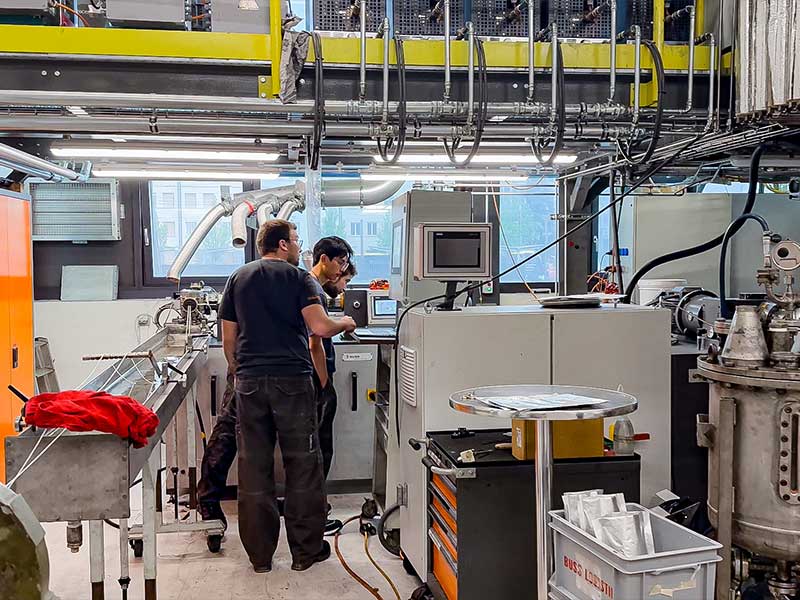 Mitarbeiter im BUSS Technikum in der Schweiz betrachten gemeinsam Testergebnisse und prüfen den Compoundierablauf im Process Engineering vor Ort.
